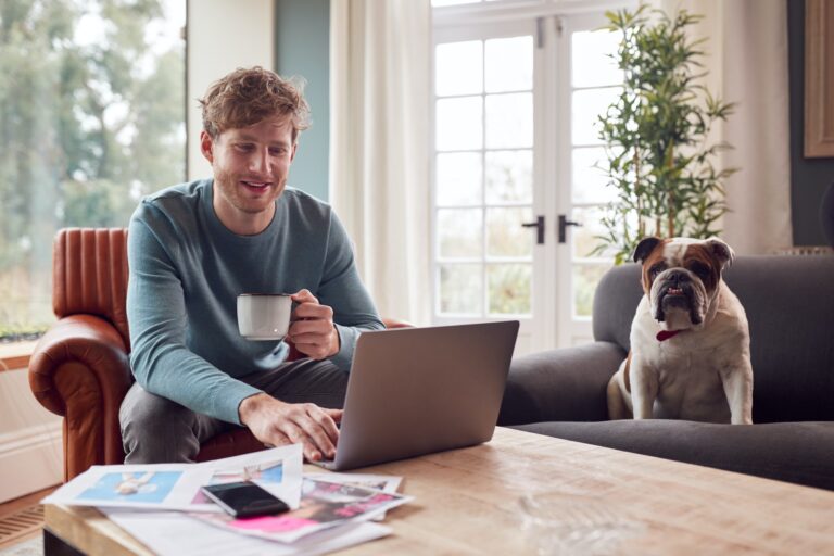Man Working From Home In Creative Design Or Marketing Industry Checking Artwork With Pet Bulldog
