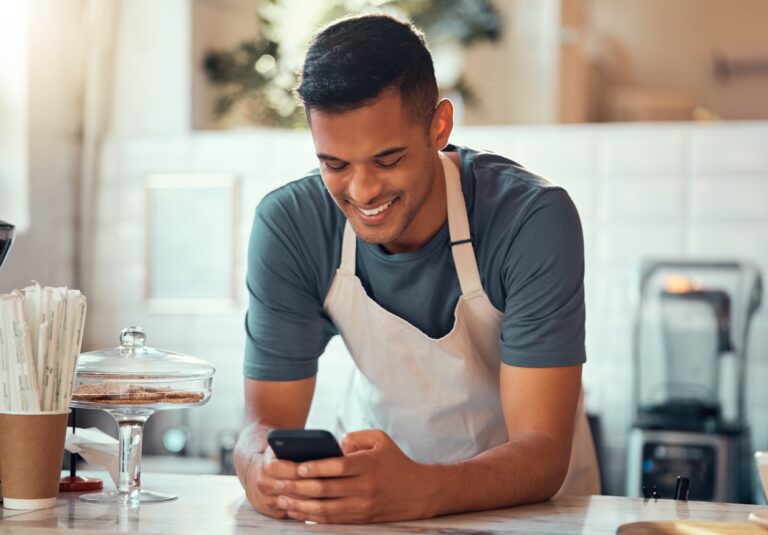 Phone, small business and barista man in cafe shop for networking, online sales management and ecom
