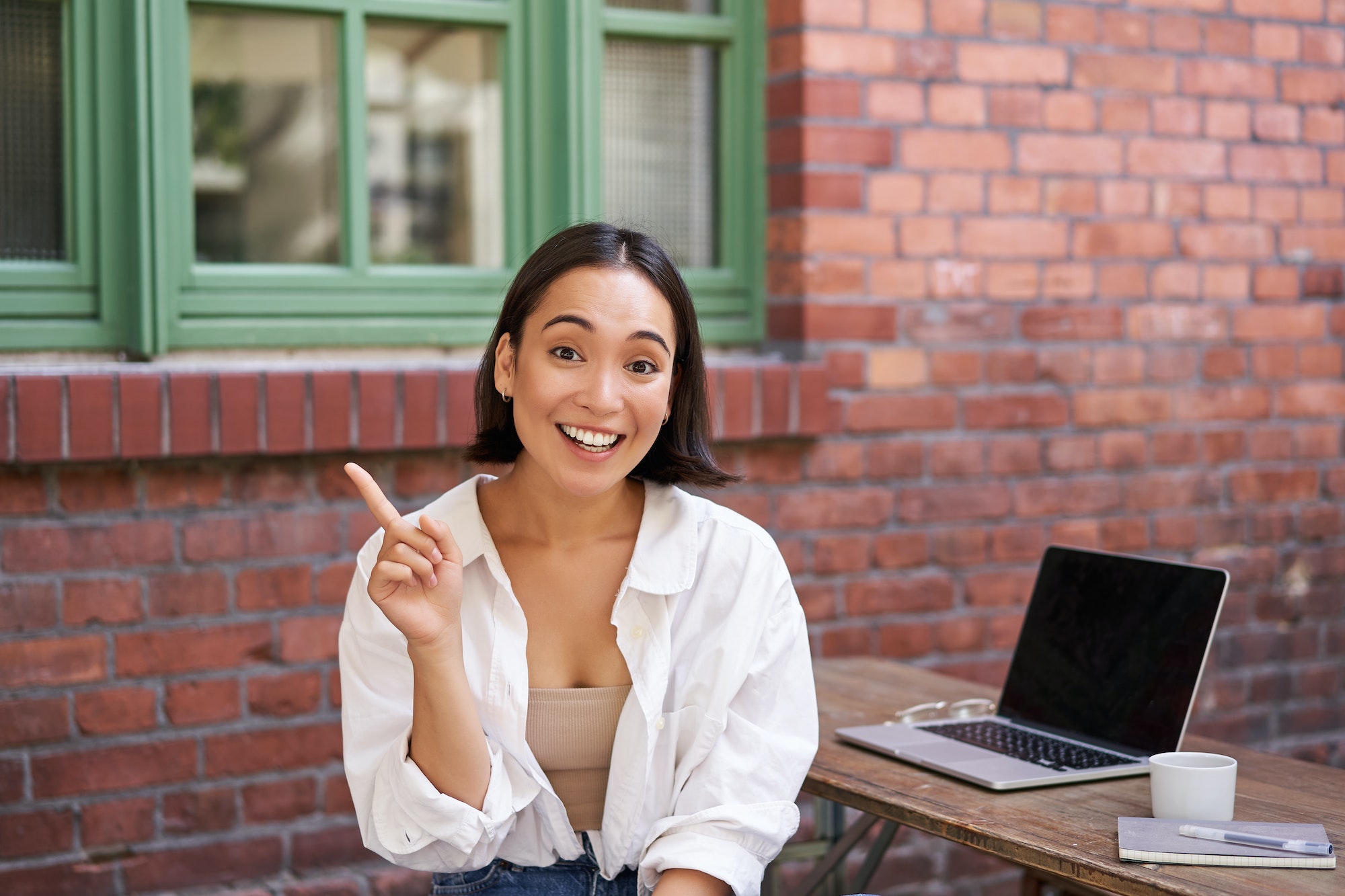 Asian girl with surprised face, sitting with laptop, pointing left at copy space, banner with